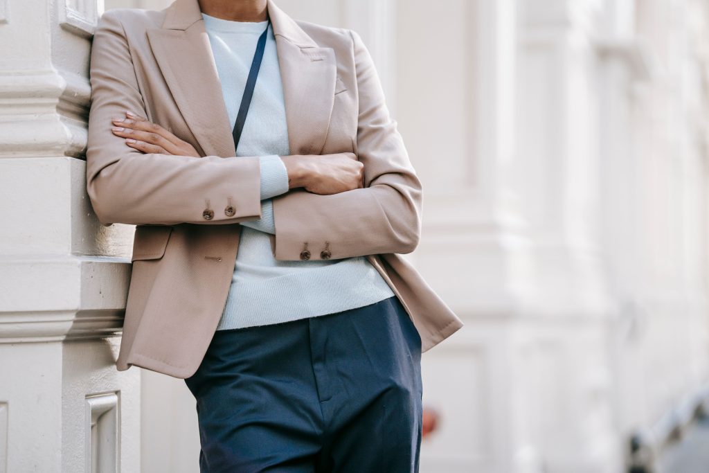 Vrouw in beige blazer leunt tegen gebouw