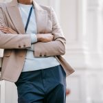Vrouw in beige blazer leunt tegen gebouw