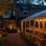 Partytent met lichtslingers en houten tafels in een tuin