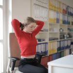 Vrouw in rode trui strekt zich uit aan bureau